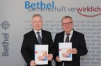 Pastor Ulrich Pohl (r.) und Dr. Rainer Norden mit dem aktuellen BethelJahresbericht 2018/2019. (Foto: Bethel)