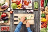 Man cooking and slicing fresh vegetables on a rustic kitchen worktop, healthy eating concept, flat lay